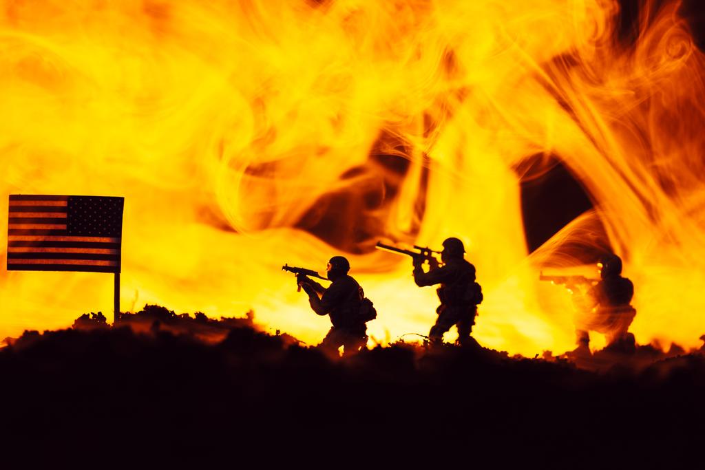 Battle scene with toy warriors near american flag with fire at background - Photo, Image