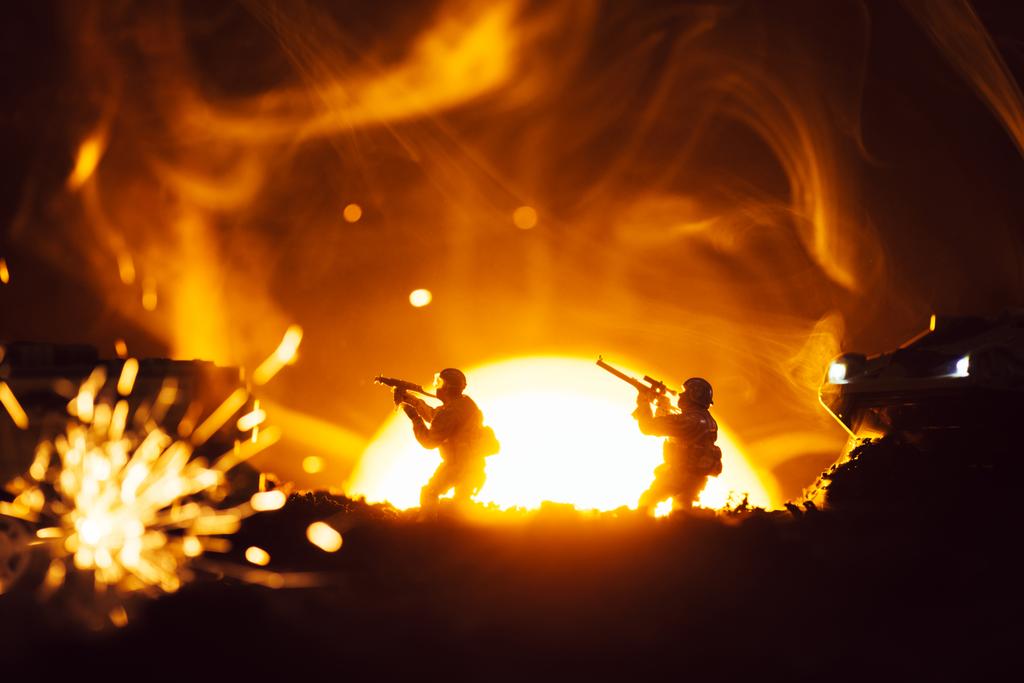 Selektywne skupienie wojowników zabawki ze zbiornikami w pobliżu wybuchu i dymu z zachodem słońca na tle - Zdjęcie, obraz