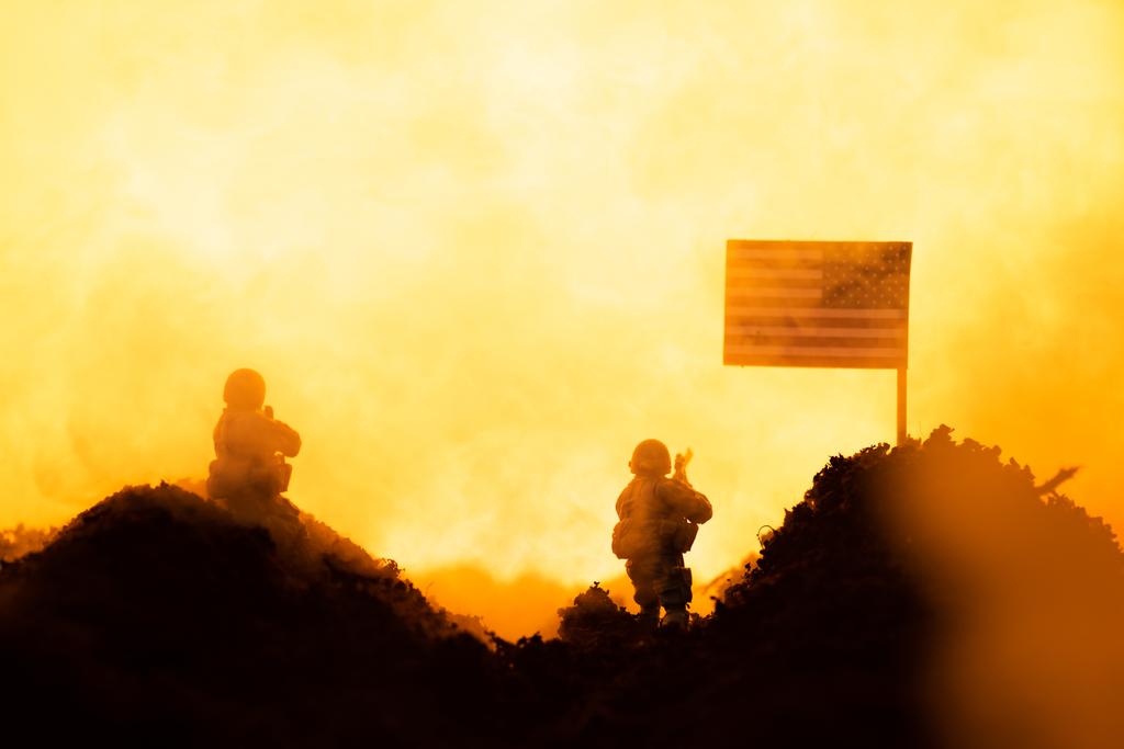 Σκηνή μάχης με στρατιώτες παιχνίδι κοντά αμερικανική σημαία με φωτιά στο παρασκήνιο - Φωτογραφία, εικόνα