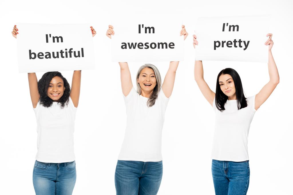 happy multicultural women holding posters with lettering above head isolated on white  - Photo, Image