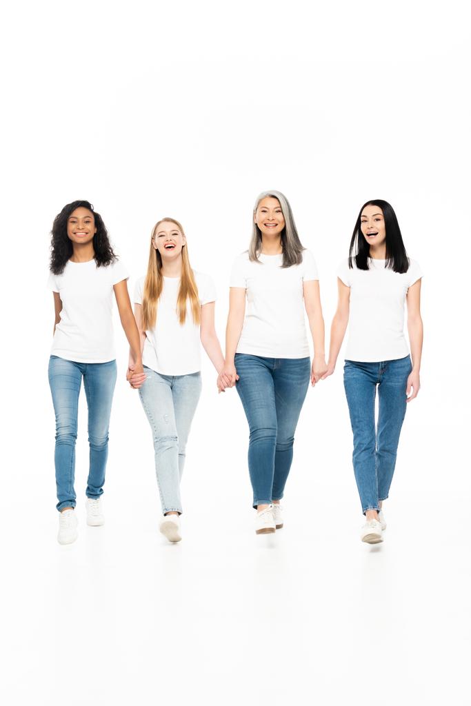 щасливі мультикультурні жінки в джинсах, що ходять і тримають руки ізольовані на білому
  - Фото, зображення
