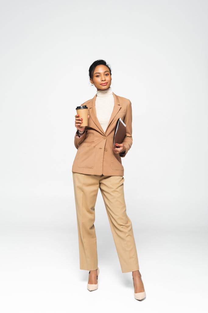 atractiva mujer de negocios afroamericana sosteniendo carpeta y taza de papel en blanco
  - Foto, imagen