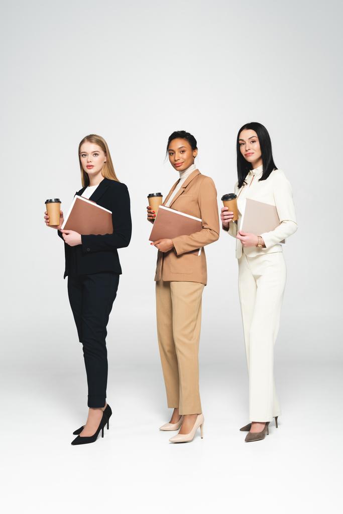 multicultural businesswomen holding disposable cups and folders on white  - Photo, Image
