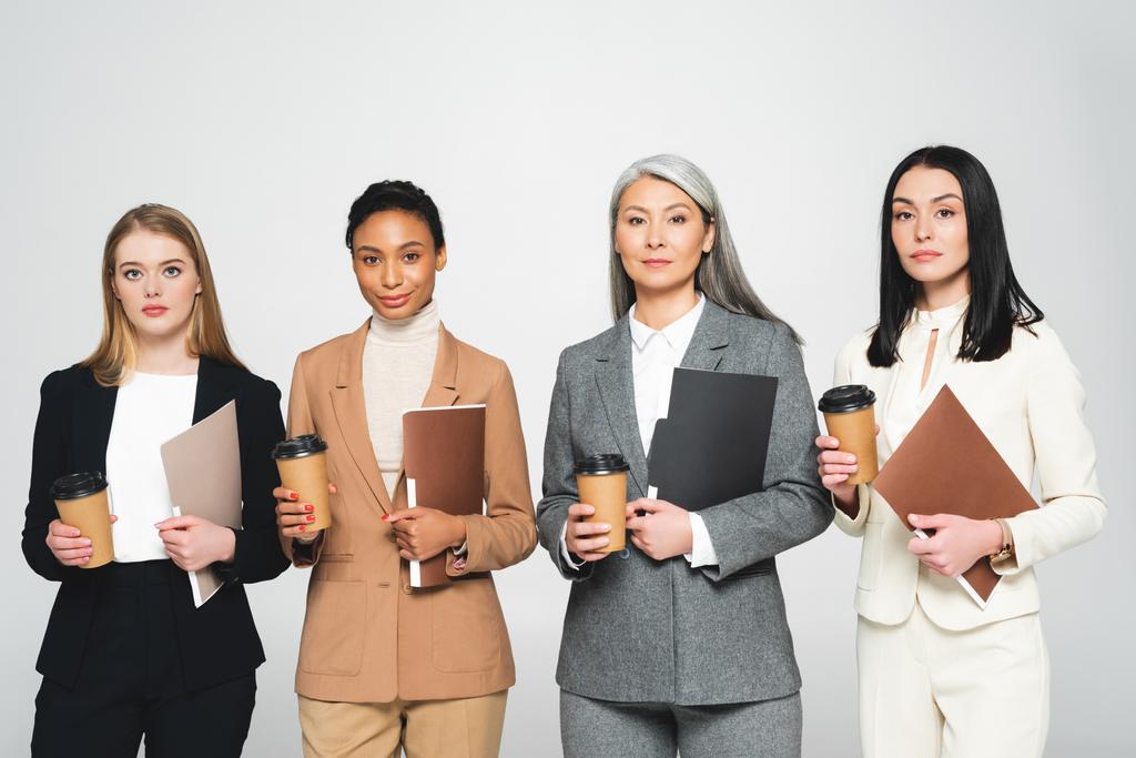 vier multiculturele zakenvrouwen met mappen en papieren bekers geïsoleerd op wit  - Foto, afbeelding