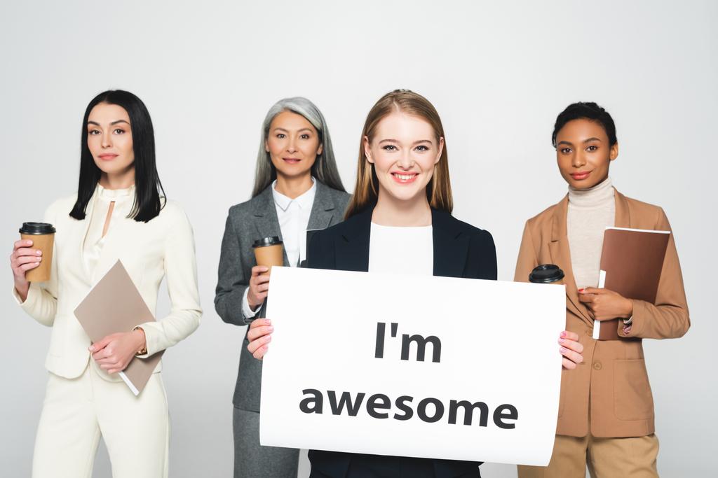 Multikulti-Geschäftsfrauen halten Ordner und Einwegbecher in der Nähe von Plakaten mit dem Schriftzug "I 'm awesome" in die Höhe.  - Foto, Bild