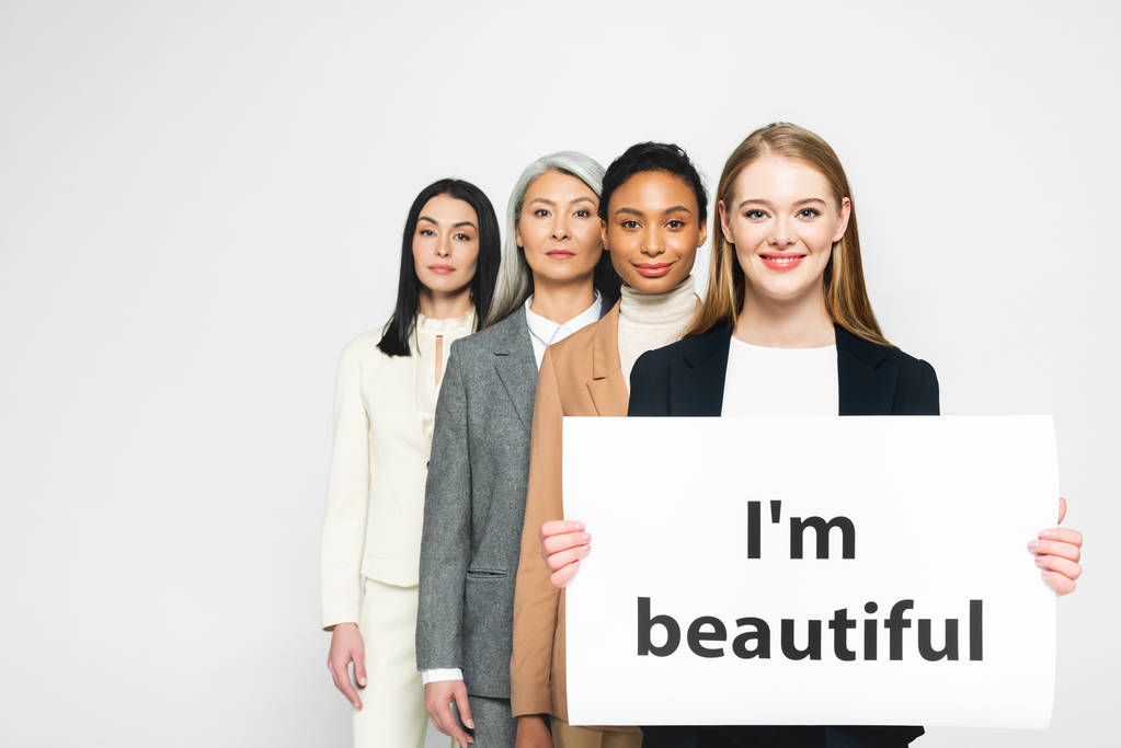 Lächelnde multikulturelle Geschäftsfrauen in der Nähe eines Plakats mit einem schönen Schriftzug auf weißem Grund  - Foto, Bild