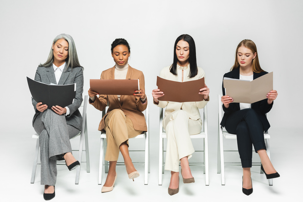 чотири мультикультурні бізнес-леді в костюмах, сидячи на стільцях і дивлячись на папки на білому
  - Фото, зображення