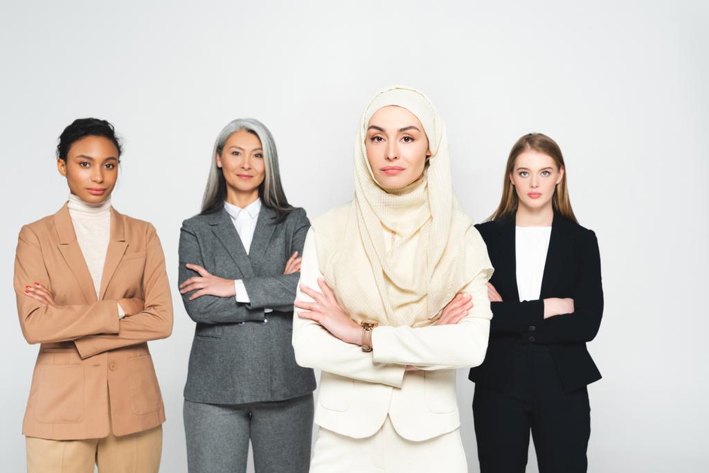 schöne multikulturelle Geschäftsfrauen stehen mit verschränkten Armen isoliert auf weiß  - Foto, Bild