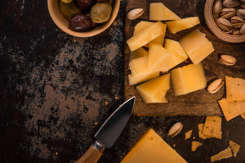 vista superior de prato de queijo com pistache, azeitonas e biscoitos na placa de corte de madeira perto da faca
 - Foto, Imagem