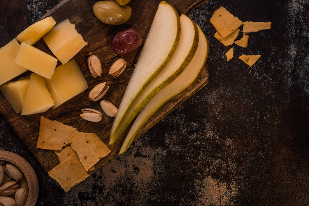 верхний вид сыра блюдо с фисташками, нарезанные груши, оливки и крекеры на выветренной поверхности
 - Фото, изображение