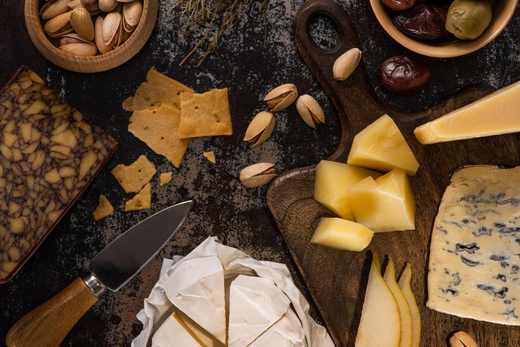 vista superior de bandeja de queijo com pistache, pêra cortada, azeitonas e biscoitos na superfície intemperizada
 - Foto, Imagem