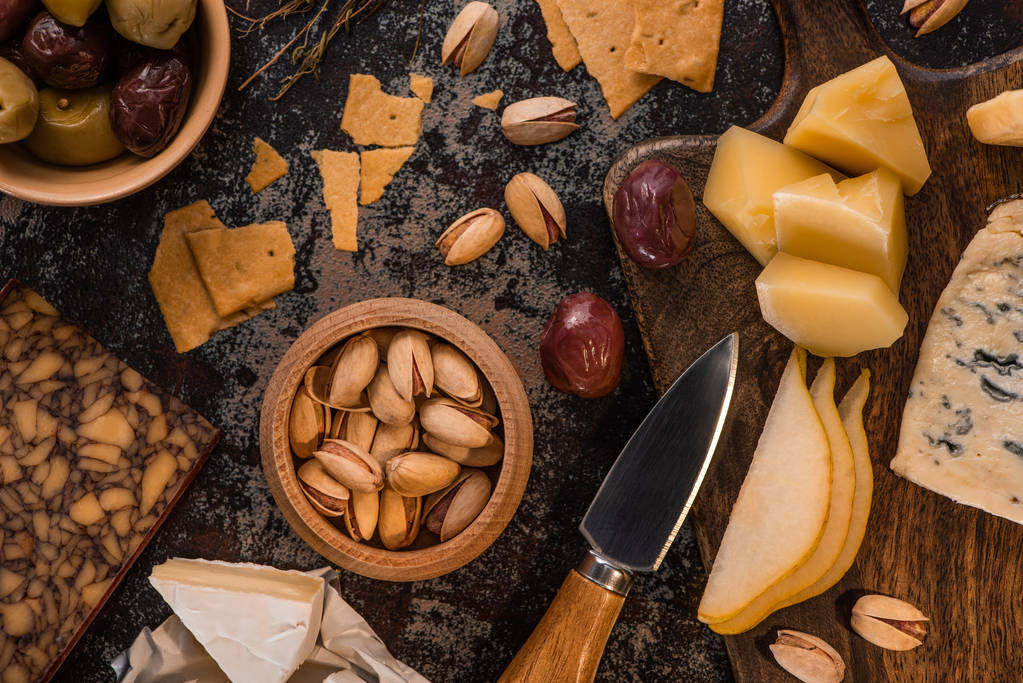 vista superior de bandeja de queijo com pistache, pêra cortada, azeitonas e biscoitos na superfície intemperizada
 - Foto, Imagem