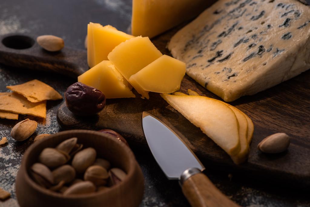 vista de cerca de bandeja de queso con cuchillo, pera en rodajas, pistachos, aceitunas y galletas saladas
 - Foto, Imagen