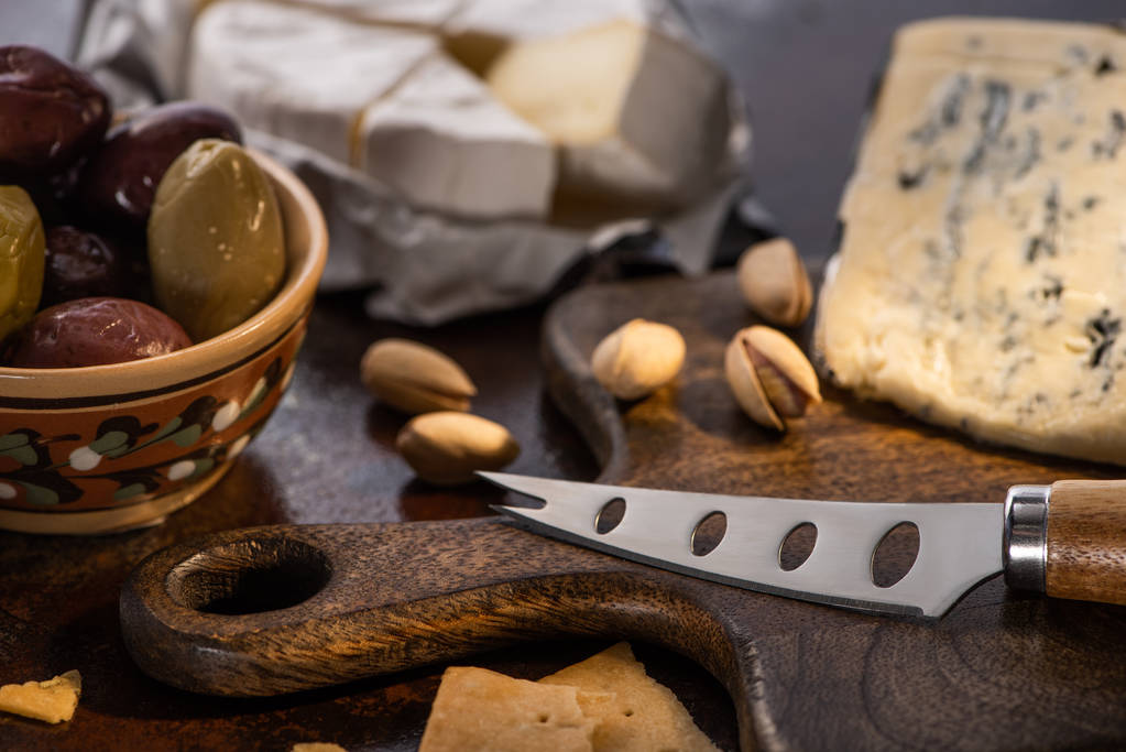 enfoque selectivo de dorblu y queso brie con aceitunas y pistachos cerca de cuchillo
 - Foto, imagen