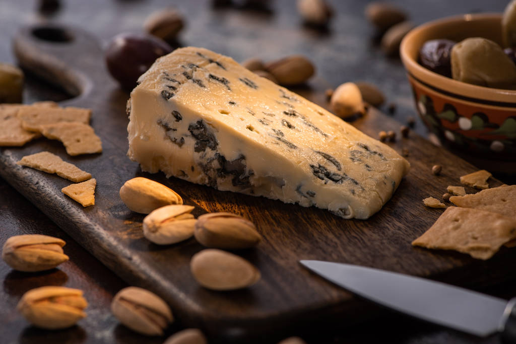 selective focus of cheese platter with dorblu, olives, crackers and pistachios near knife - Photo, Image