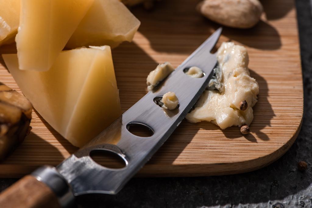 Selective focus of soft dorblu pressed by knife next to pieces of grana padano on cutting board - Photo, Image