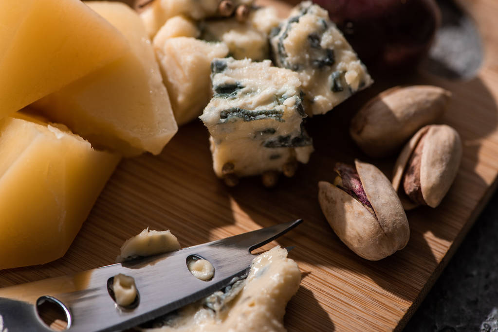Enfoque selectivo de dorblu prensado por cuchillo junto a piezas de grana padano y pistachos en tabla de cortar
 - Foto, Imagen