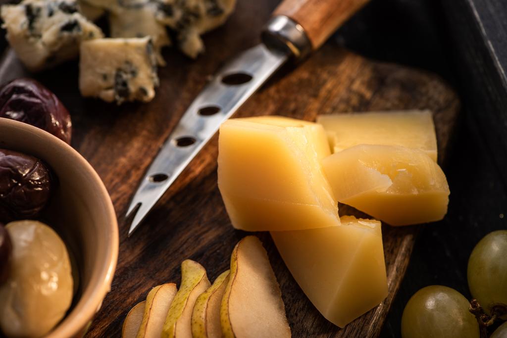 Селективный фокус Грана Падано с ножом, ломтиками груши, оливок, винограда и dorblu на разделочной доске
  - Фото, изображение