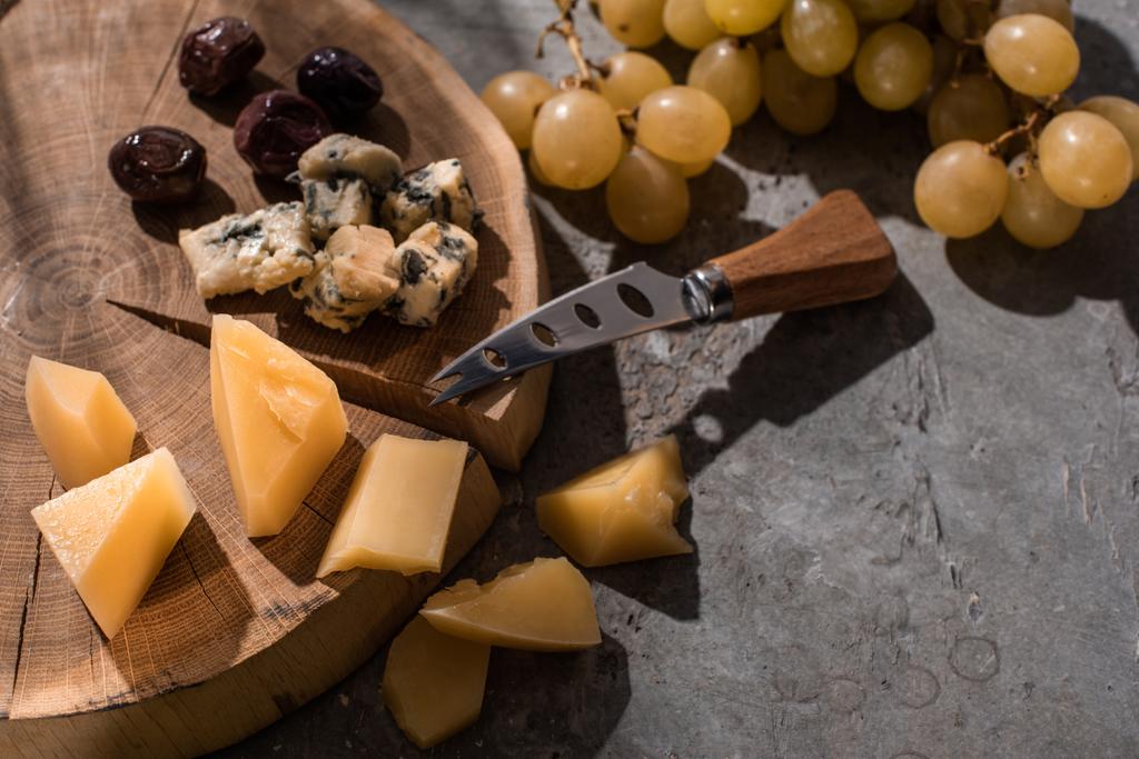 Grana padano and dorblu with olives and knife on wooden board next to grapes on grey background - Photo, Image