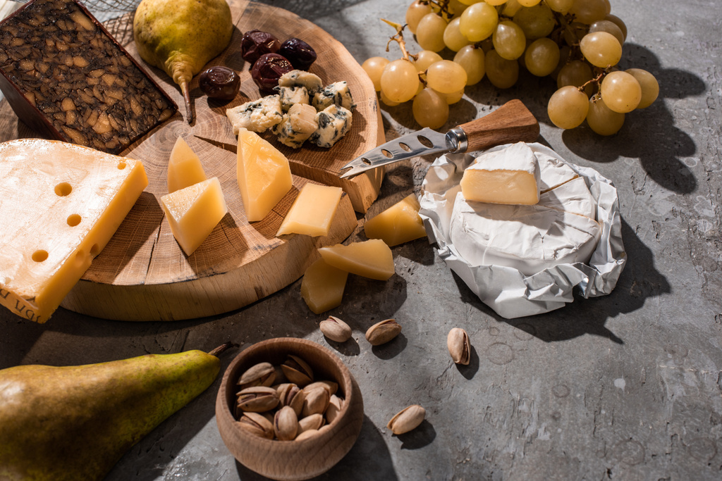 Verschillende soorten kaas met fruit, olijven, pistachenoten, op houten plank op grijze ondergrond - Foto, afbeelding