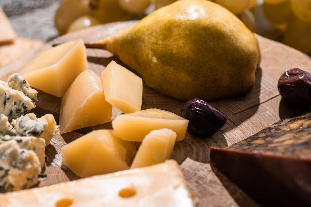 Selective focus of different kinds of cheese with dried olives and pear on round wooden board - Photo, Image