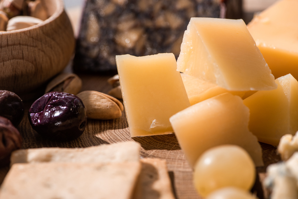 Selective focus of grana padano, crackers, olives and pistachios on wooden background - Photo, Image