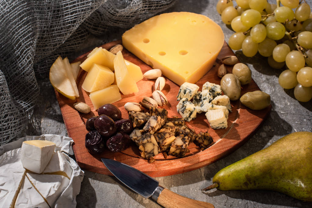 Pera, Camembert, uvas y cuchillo junto a tabla de cortar con composición de alimentos sobre fondo gris
 - Foto, imagen