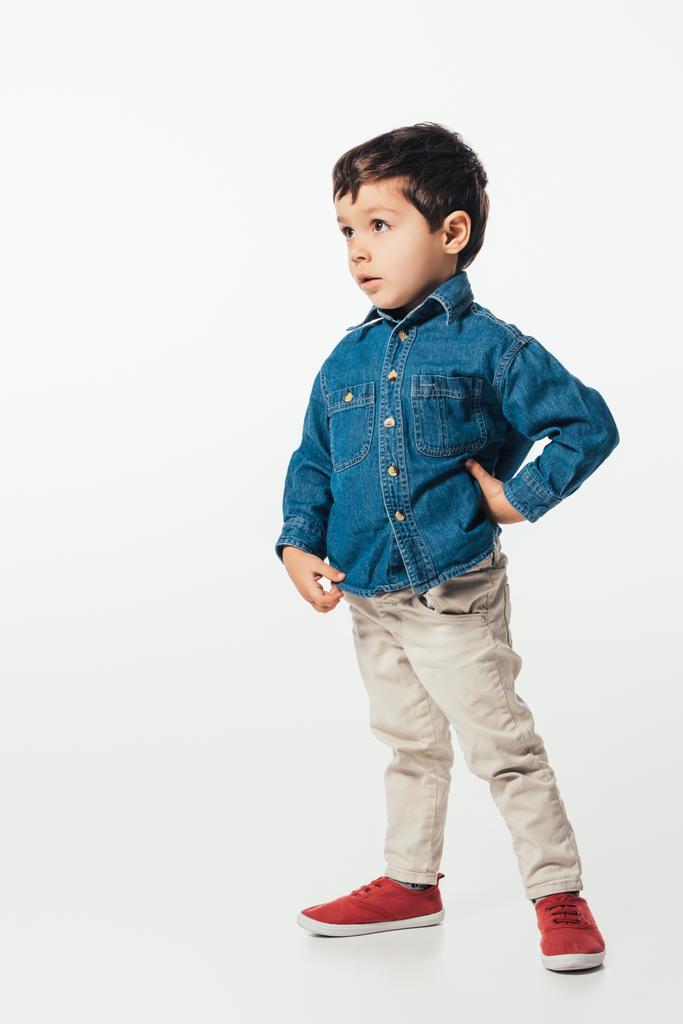šokovaný chlapec v džínové košili s rukou na boku dívá pryč na bílém pozadí  - Fotografie, Obrázek
