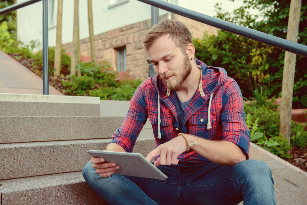 jeune homme en chemise à carreaux assis sur les escaliers et en utilisant tablette PC
 - Photo, image
