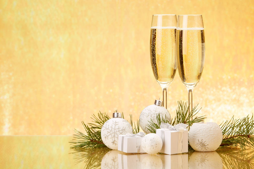 シャンパン、モミの木の枝、ギフトボックス、黄金の背景にクリスマスの装飾が施された2つのメガネ。お正月とクリスマス. - 写真・画像