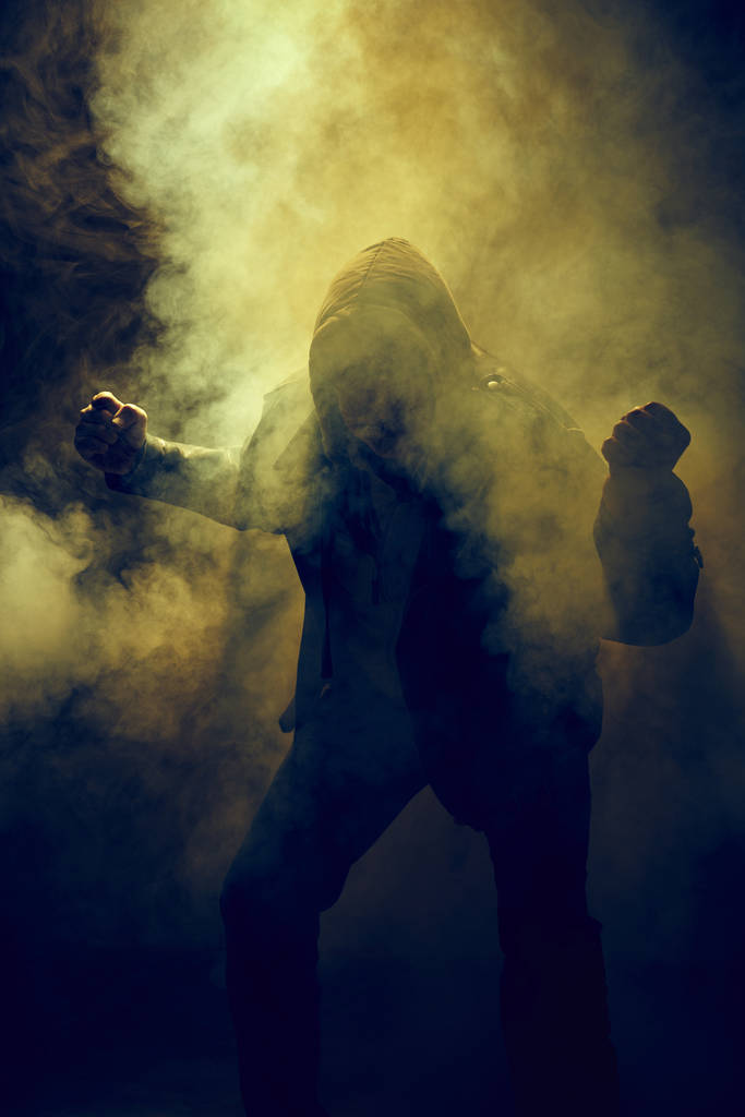 Faust und Hand eines Mannes in Lederjacke und Kapuzenpullover im Nebel gegen das Licht - Foto, Bild