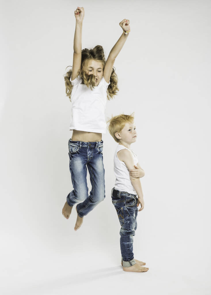 Студійний портрет хлопчика, що стоїть і сестра стрибає середнє повітря
 - Фото, зображення