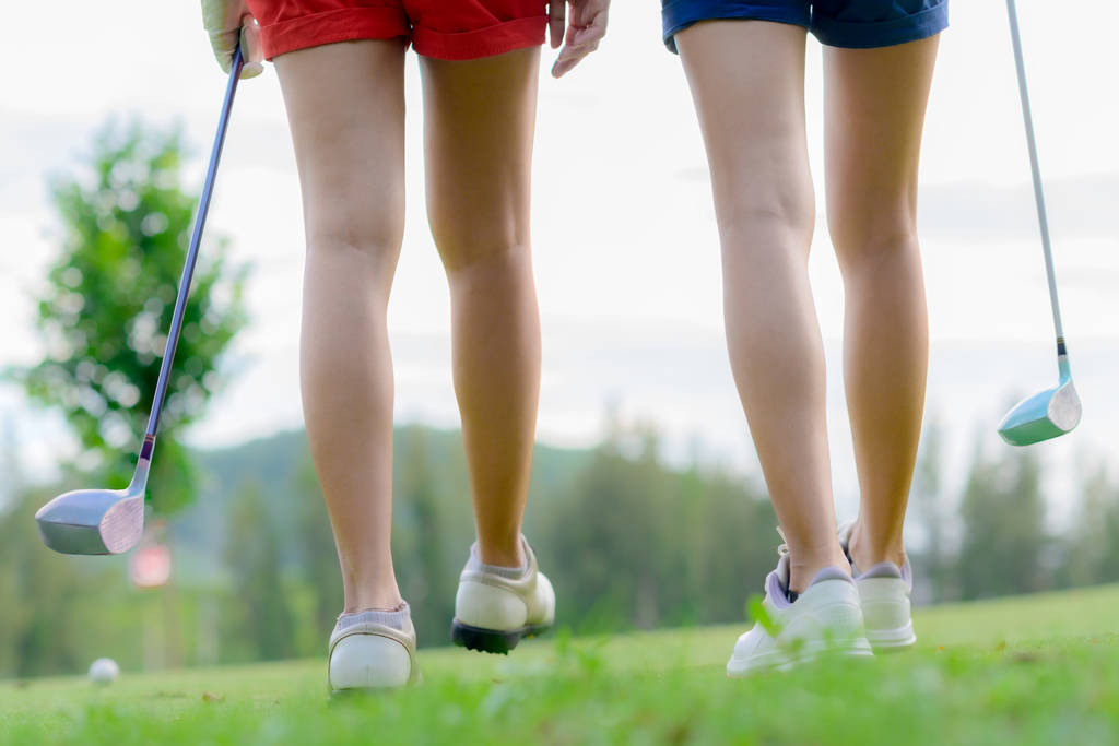 πόδια της νεαρής γυναίκας παίκτες του γκολφ και οι δύο με τα πόδια σε T-Off για να λάβει την επόμενη βολή χτύπησε την μπάλα στο δίαυλο προορισμού - Φωτογραφία, εικόνα