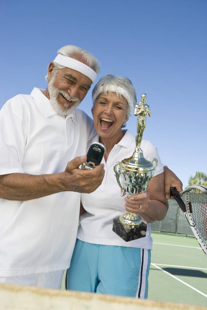 Izgalmas nyugdíjas pár trófeával, akik mobilon készítenek önarcképet a teniszpályán - Fotó, kép