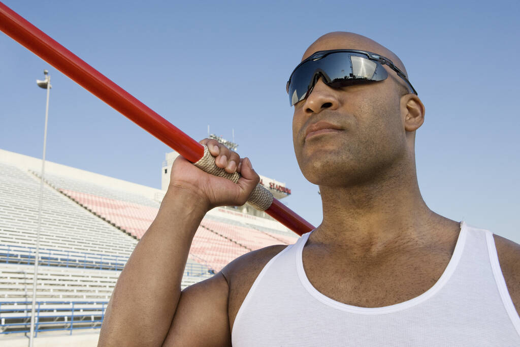 Афроамериканский спортсмен собирается бросить копье с трибуной на заднем плане
 - Фото, изображение