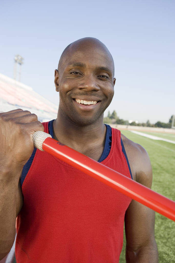 Retrato de feliz atleta masculino afro-americano segurando dardo no estádio
 - Foto, Imagem