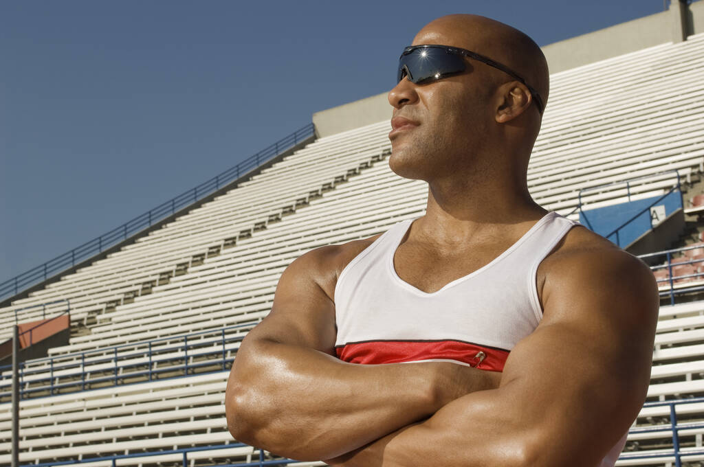 Atleta masculino confiante vestindo óculos de sol com braços cruzados no estádio
 - Foto, Imagem