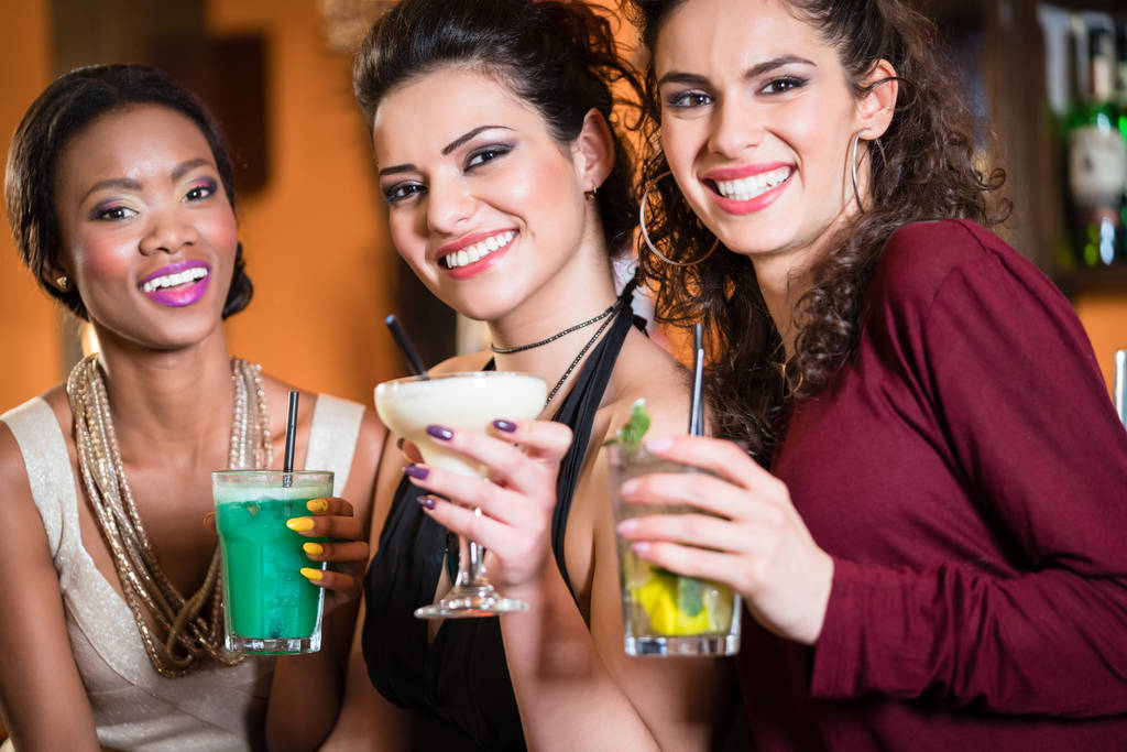Beautiful girls in nightlife drinking cocktails and saying Cheers - Photo, Image