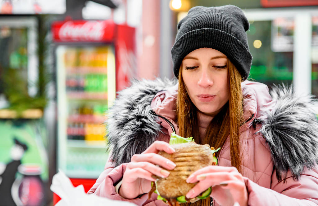 Utcai kaja. fiatal nő kezében szaftos ciabatta szendvics és eszik szabadban tél - Fotó, kép