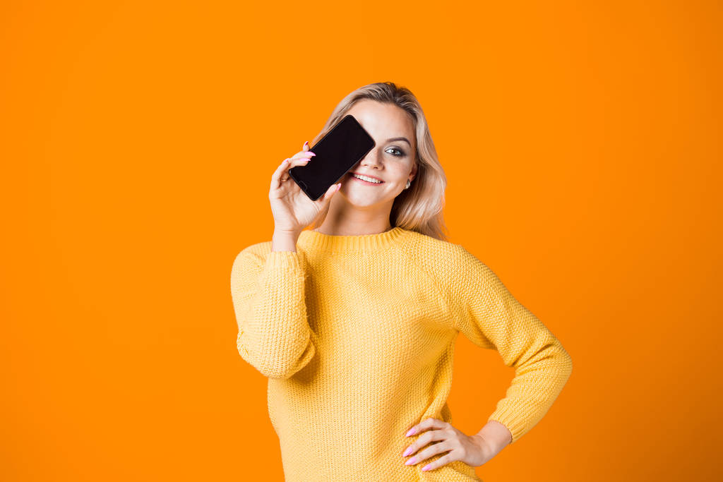Jeune femme mignonne dans un pull jaune tenant un smartphone
 - Photo, image