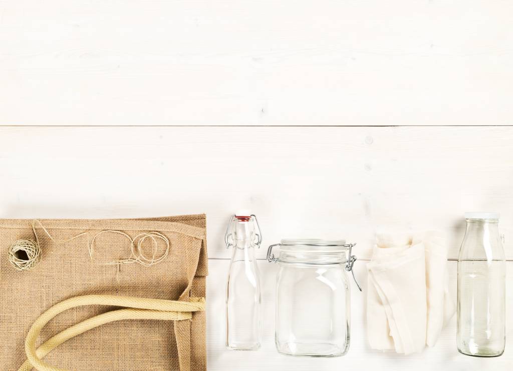 Çuval bezi, cam şişeler ve beyaz ahşap masa üzerinde pamuk torbası olan sıfır atık ya da atıksız alışveriş aletleri - Fotoğraf, Görsel