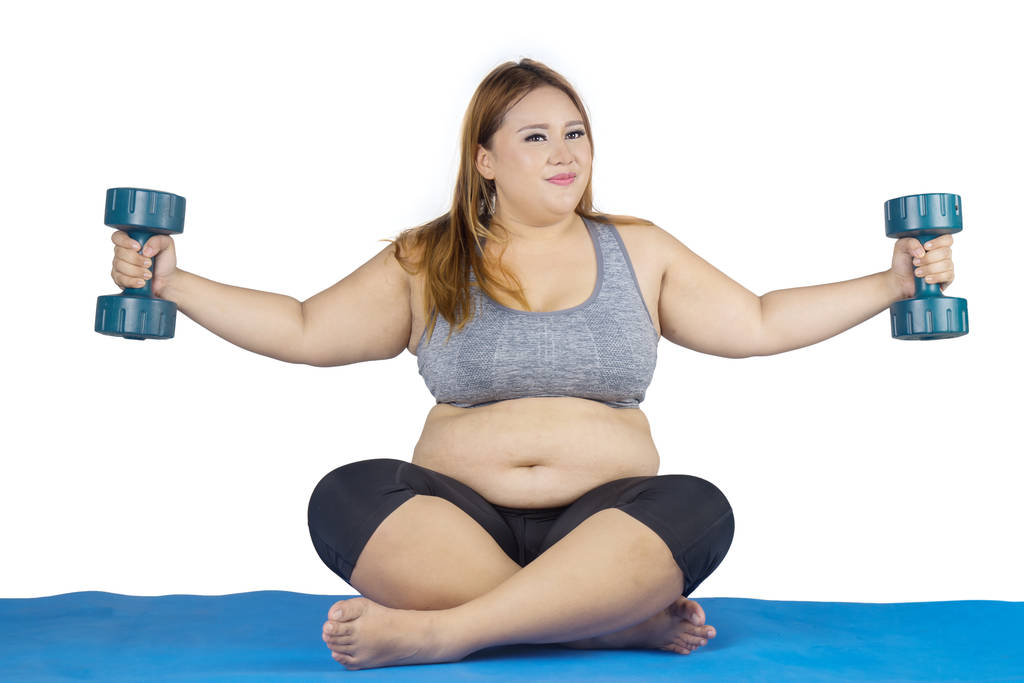 Obese woman doing exercise with dumbbells on mat - Photo, Image