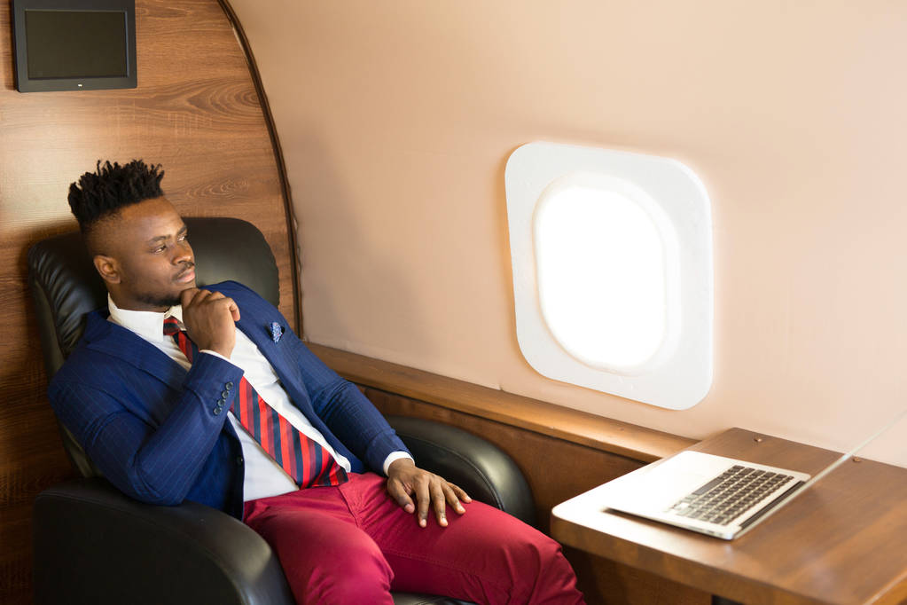 bello africano giovane in tuta in cabina jet privato con computer portatile
 - Foto, immagini