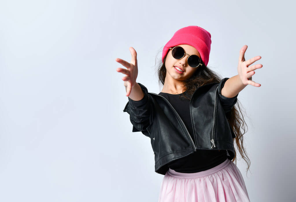 Подросток в кожаной куртке, розовой шляпе и солнцезащитных очках. Она улыбается, тянет руки к тебе, изолированная на белом. Закрыть
 - Фото, изображение