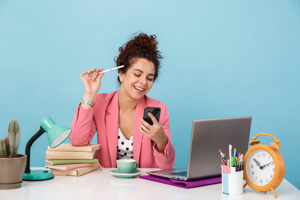 Kuva nauraa brunette nainen käyttää matkapuhelinta työskennellessään työpöytä
 - Valokuva, kuva