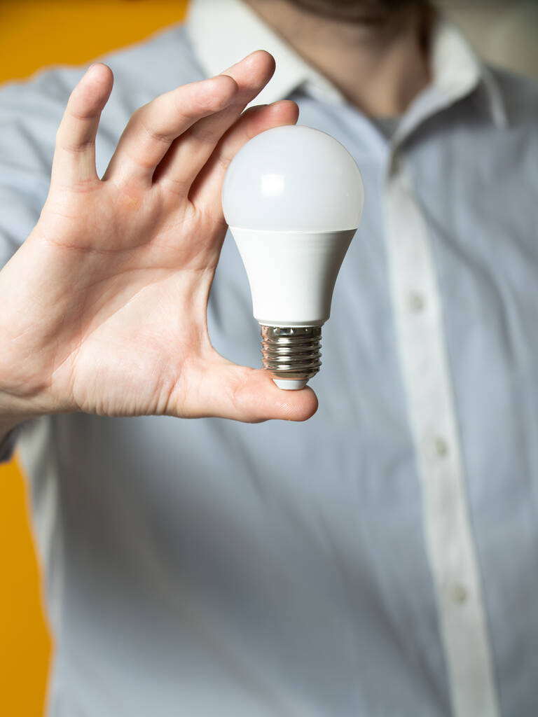 La main d'un homme tenant une ampoule pour l'innovation et concept créatif. Ampoule à la main sur fond jaune. Espace vide pour votre texte
 - Photo, image