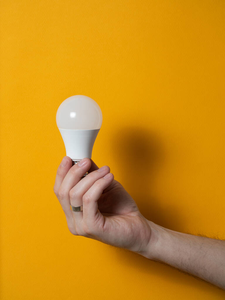 A mão de um homem segurando uma lâmpada para inovação e conceito criativo. Lâmpada na mão sobre um fundo amarelo. Espaço vazio para o seu texto
 - Foto, Imagem