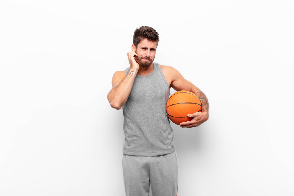 młody przystojny mężczyzna czuje się zestresowany, sfrustrowany i zmęczony, pocierając bolesną szyję, ze zmartwionym, niespokojnym spojrzeniem trzymającym piłkę do koszykówki. - Zdjęcie, obraz