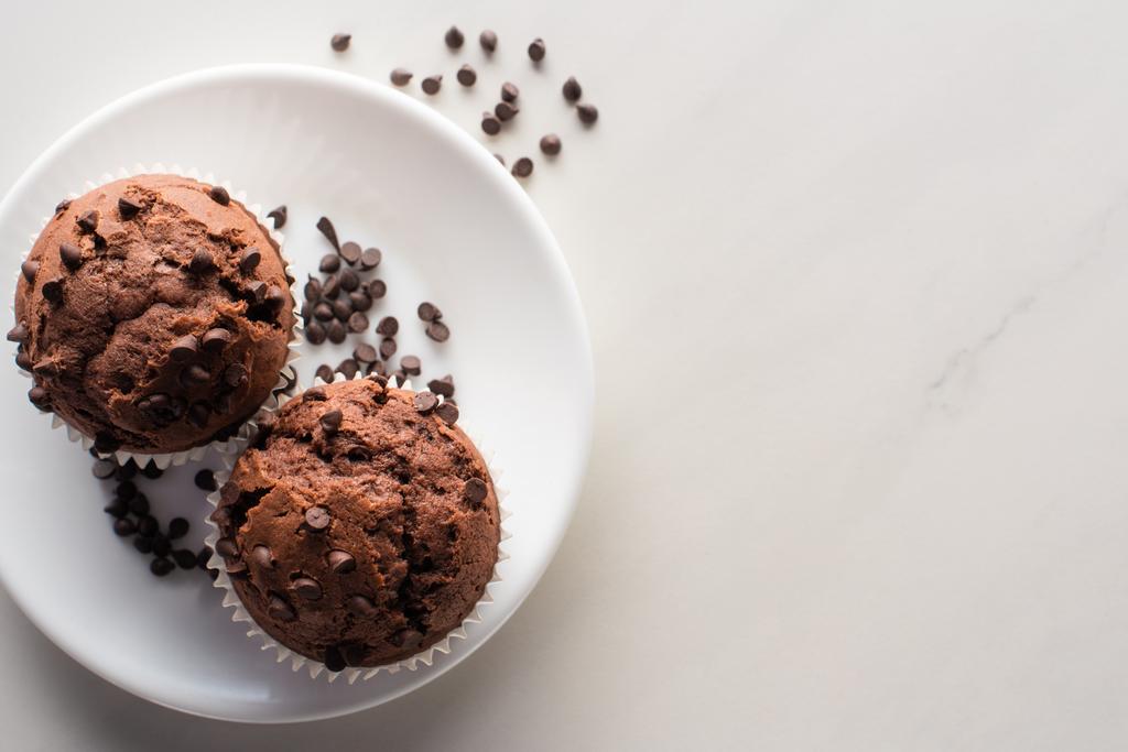 top view of fresh chocolate muffins on white plate on marble surface - Fotoğraf, Görsel