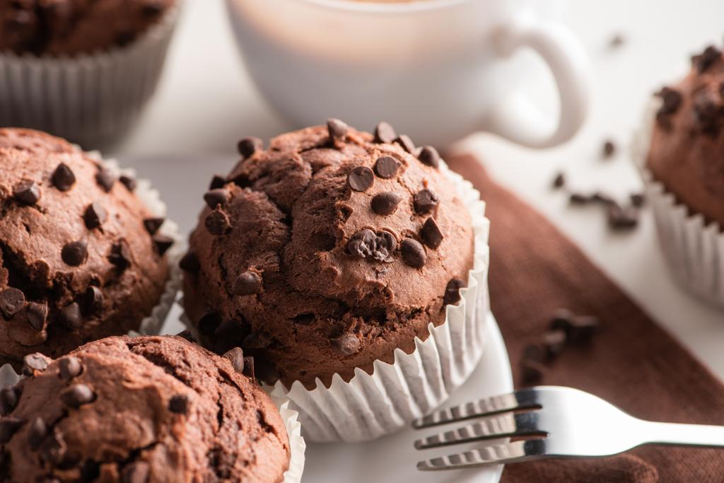 close up view of fresh chocolate muffins on white plate near fork - Photo, Image